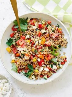 a white bowl filled with rice and vegetables next to a wooden spoon on top of a table