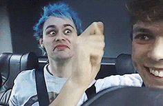 two young men sitting in the back seat of a car, one with blue hair