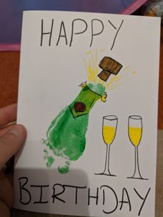 a hand holding up a birthday card with an image of a bottle and two glasses