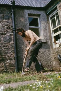 a shirtless man holding a shovel in front of a building