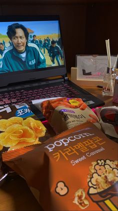 an open laptop computer sitting on top of a wooden table next to snacks and drinks