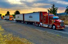 a red semi truck driving down the road with other trucks behind it on either side