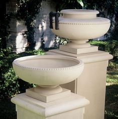 three white urns sitting on top of each other in front of bushes and trees