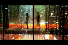 two people are walking in front of some glass doors with rain drops on the floor