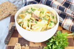 a white bowl filled with pasta on top of a wooden cutting board next to crackers