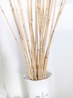 a white vase filled with bamboo sticks on top of a table next to a wall