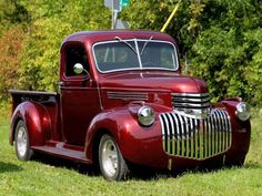 an old red truck is parked in the grass