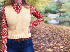 a woman standing in front of trees with her hands on her hips wearing a sweater and jeans