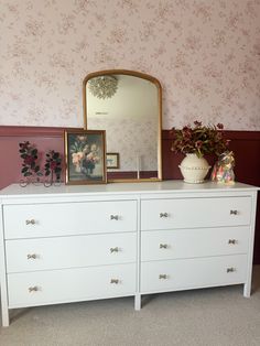 a white dresser with two vases on top and a mirror above it in a pink room