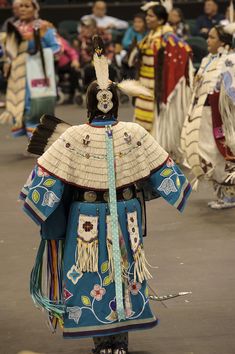 some people are dressed in native clothing and dancing with feathers on their head as they walk down the street