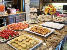 a kitchen counter topped with lots of trays filled with different types of cookies and pastries