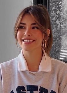 a smiling woman with large hoop earrings in front of a window