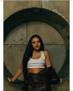 a woman with long black hair is posing in front of a circular wall and wearing leather pants