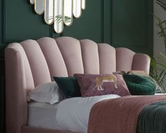 a bed with pink headboard and pillows in a green room next to a mirror