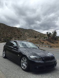 a black car is parked on the side of the road in front of a hill