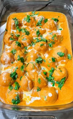 a casserole dish with meatballs and cheese in orange sauce, garnished with parsley