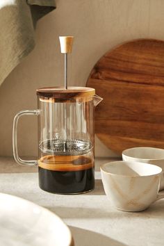 a glass coffee maker sitting on top of a counter next to two bowls and a wooden board