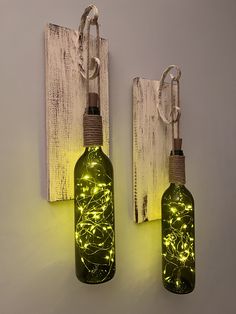 two bottles with lights attached to them are hanging on the wall next to each other