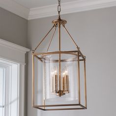 a light fixture hanging from the ceiling with three candles in it and one candle lit