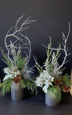 three vases with plants and pine cones on a black surface, one has white flowers in it