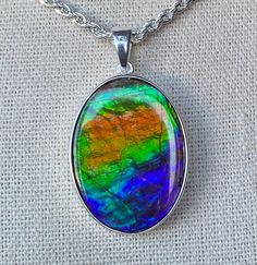 "This Ammolite pendant has a lovely gem in orange, green and blue.  This gem is a large calibrated freeform measuring in at 25mm x 18mm.   It comes on an 18\" silver plated chain as shown.  Other lengths available on request, but keep in mind that the gem shows off its color best when worn high on the neck.  Please remember that I offer combined shipping." Multicolor High Luster Necklace For Gift, Multicolor High Luster Necklaces As Gift, Multicolor Oval Jewelry With Natural Inclusions, Iridescent Oval Gemstone Necklace, Oval Multicolor Gemstones For Gift, Iridescent Oval Gemstone Necklaces, Multicolor Large Gemstones For Gift, Gem Show, Green And Blue