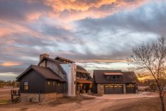 a large house sitting in the middle of a dirt road under a cloudy sky at sunset