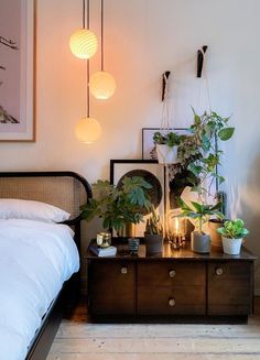 a bedroom with plants on the nightstand and lights hanging from the ceiling over the bed