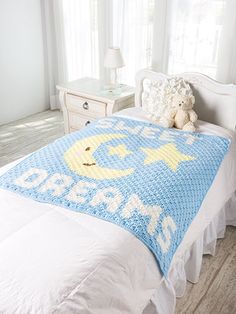 a crocheted baby blanket on a bed in a room with white furniture and windows