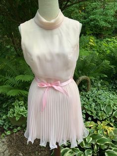 "This lighthearted cocktail dress is sooooo 60s.  Nylon organza layers atop a satin lining, and the skirt is not only pleated, but is edged at the hem with wire to keep the pleats curly.  2\" turtleneck, 20\" back zipper, and a pink satin ribbon to tie at the waist. Please note there are a few brown spots on the front of this dress. (Get those special pieces cleaned after your event, ladies!)  See the final photo.  Priced accordingly Bust 35\" - 36\" Waist 26\" Hips 40\" Length 16\" to waistline; 33\" total" Party Vintage A-line Dress With Ruffles, Feminine Party Mini Dress With Pleated Bodice, Feminine Mini Dress With Pleated Bodice For Party, Spring Party Vintage Dress In Feminine Style, Spring Vintage Feminine Dress For Party, Feminine Vintage Dress For Spring Party, A-line Pleated Dress With Ruffles For Party, Vintage Mini Dress For Wedding, Cream Vintage Dress For Spring Party