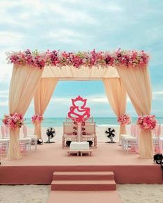 an outdoor ceremony set up on the beach with pink flowers and white draping