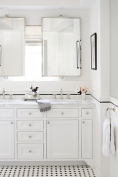 a white bathroom with black and white tile flooring, two sinks and mirrors on the wall