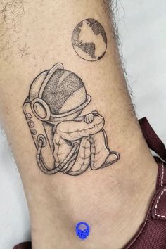 a small tattoo on the ankle of a man with an astronaut's helmet and earth