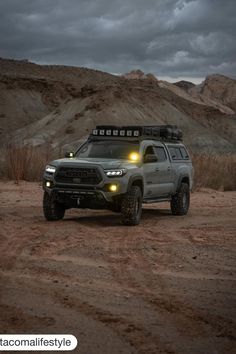 the truck is parked in the dirt with its lights on and it's hood up