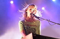 a woman standing in front of a keyboard on top of a stage with lights behind her