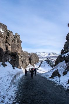 some people are walking on a path in the snow and rocks with mountains in the background