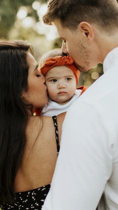 a man and woman holding a baby in their arms while they are kissing each other