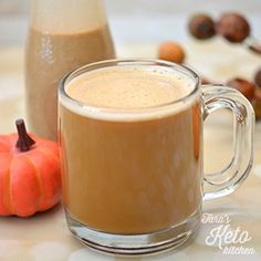 a glass mug filled with liquid next to an orange pumpkin