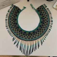 a green and gold beaded necklace sitting on top of a white table next to a pair of glasses