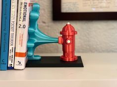 a red fire hydrant sitting on top of a book shelf next to two books