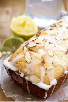 a loaf of bread with white icing and nuts on top next to sliced lemons