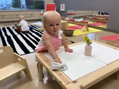 a baby sitting at a table in a classroom