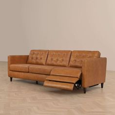 a brown leather couch sitting on top of a hard wood floor next to a wall