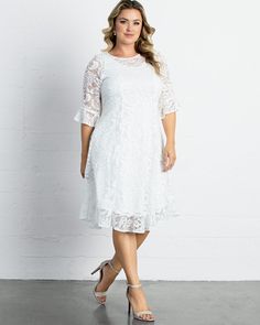 a woman wearing a white lace dress and heels standing in front of a brick wall