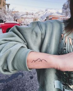 a person with a small tattoo on their arm in the snow covered mountains behind them