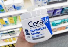 a hand holding up a jar of cerave moistizing cream in front of shelves