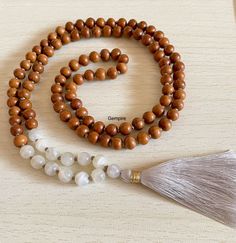 "Sandalwood and Moonstone Mala Necklace - 108 + 1 Beads in Knotted Mala with Tassel The Combination of Sandalwood and Moonstone makes the Mala look beautiful as both are Powerful Natural elements - Gifts of Nature to us. This Mala stands for Calmness, Encouragement, Emotional Balance and New Beginnings Sandalwood is a very sacred wood and used widely in Puja/prayer. It has many medicinal properties. It creates a soothing atmosphere around us. It reduces stress and generates positivity. Prayers u Wooden Round Beads Jewelry For Meditation, Brown Mala With Natural Stones And Round Beads, Brown Mala With Natural Round Beads, Brown Mala With Natural Stones, Sandalwood Mala, Knotted Mala, Yoga Mala, Buddhist Prayer, Wood Bead Necklace