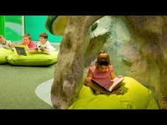 children are sitting on bean bags and reading books in an indoor play area with trees