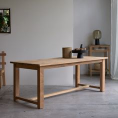 a wooden table sitting on top of a cement floor next to a chair and potted plant