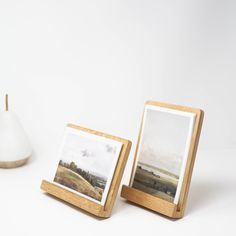 two wooden frames sitting next to each other on top of a white table with a vase in the background