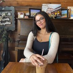 a woman sitting at a table with a drink in front of her and a sign on the wall behind her